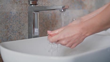 Close-up-of-woman-washing-hands-in-the-bathroom-sink.