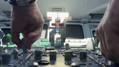 closeup view, low angle shot, of the hands of two white pilots performing routine procedures in a jet cockpit bathed by the sunlight. captain is wearing bracelets and a ring