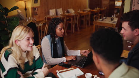group of friends gathered at a restaurant with a laptop