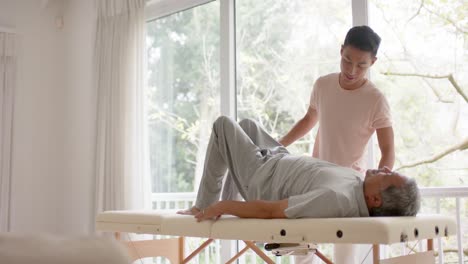 다양한 남성 물리치료사가 조언하고 노인 남성 환자가 소파에서 느린 동작으로 운동합니다.