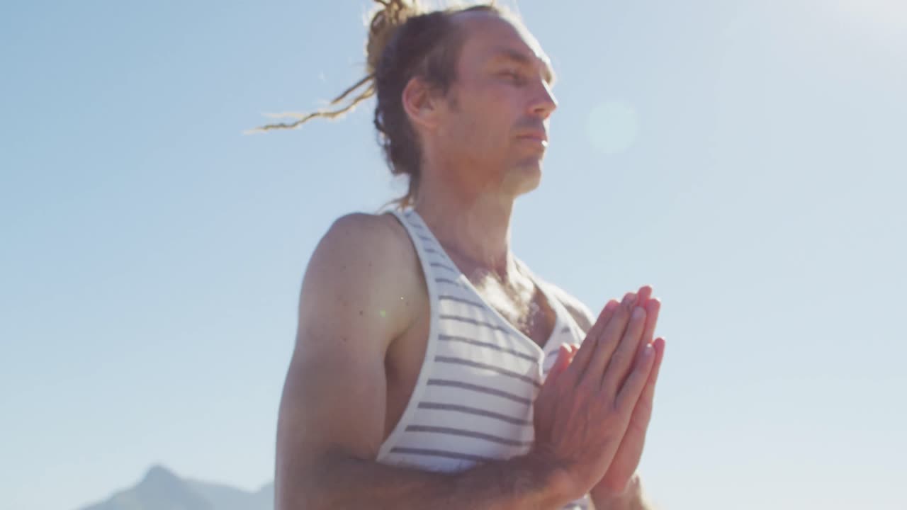 Video: Glücklicher kaukasischer Mann mit Dreadlocks praktiziert Yoga-Meditation sitzend im Freien in der Sonne.