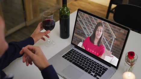 Mixed-race-man-sitting-at-table-using-laptop-making-video-call-with-female-friend