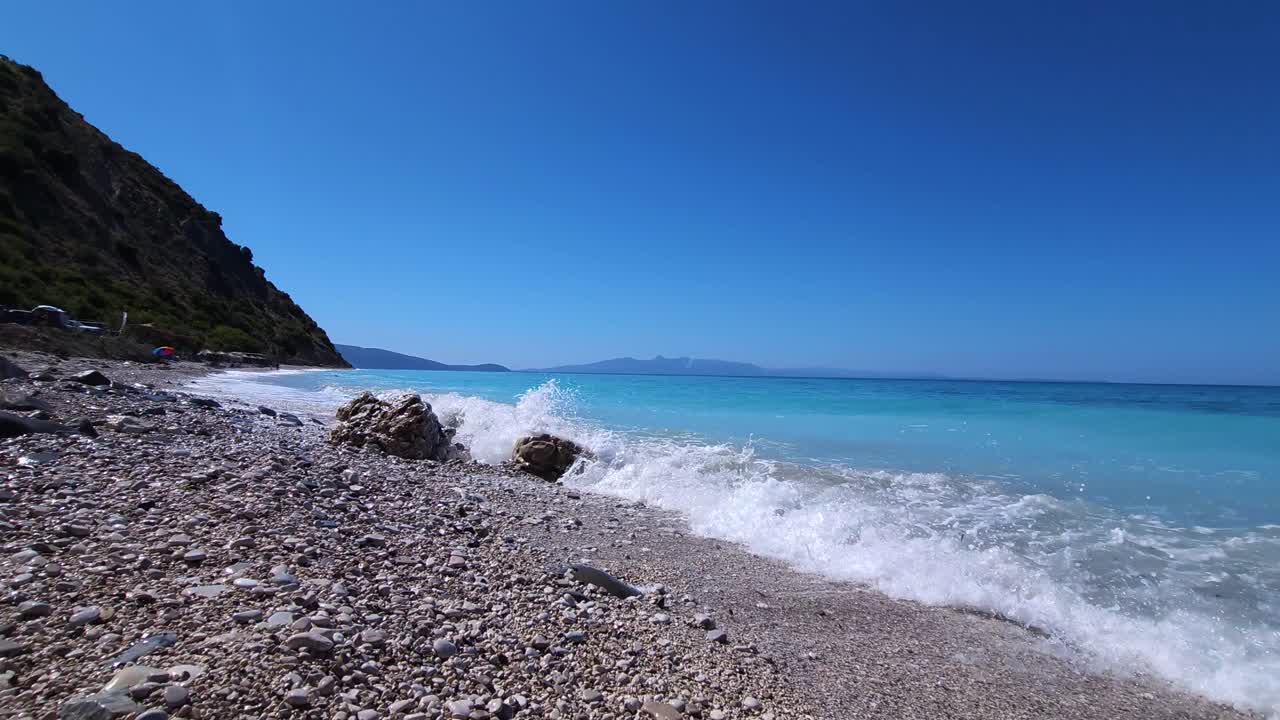 Walking on pebbles of paradise beach washed by white sea waves on beautiful seaside with mountains and blue turquoise seawater in Albania