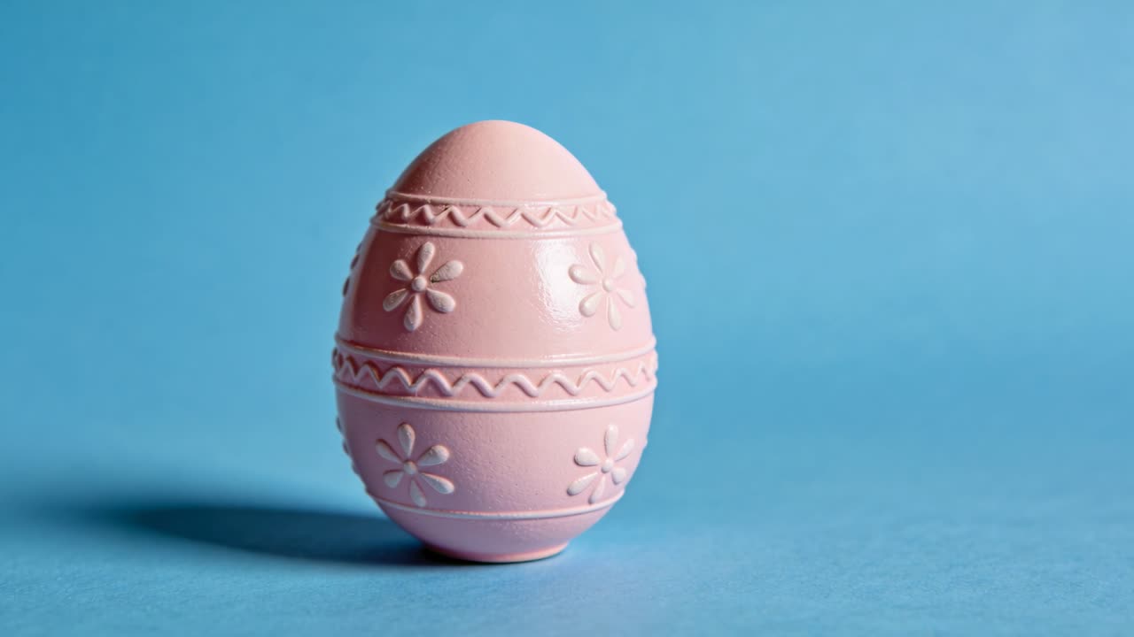 Camera zooming toward pink egg-shaped object on blue tabletop, revealing embossed floral bands