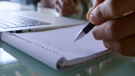 man writing on notepad while using laptop at home 4k