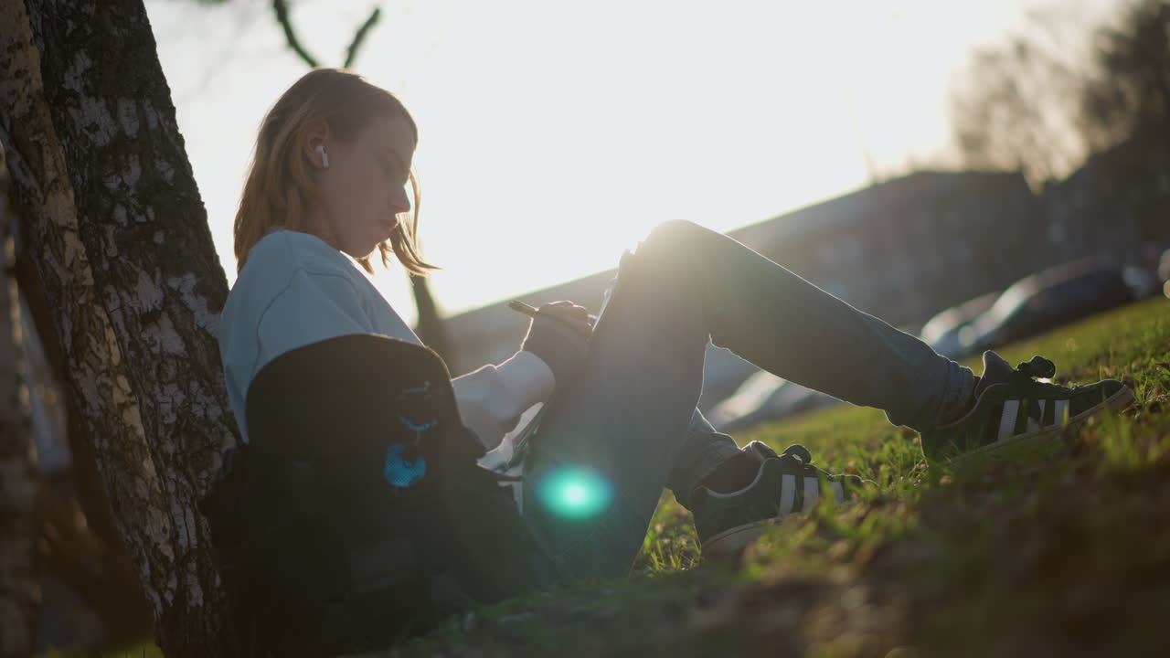 젊은 여성이 공원에서 휴식을 취하고 있어요. 한 여성이 나뭇잎이 무성한 덮개 아래에서 책을 읽으며 평화로운 오후를 즐기고 있습니다. 젊은 여성은 야외 환경에서 넓게 펼쳐진 나뭇가지 아래에서 평화롭게 독서에 몰두하고 있어요.