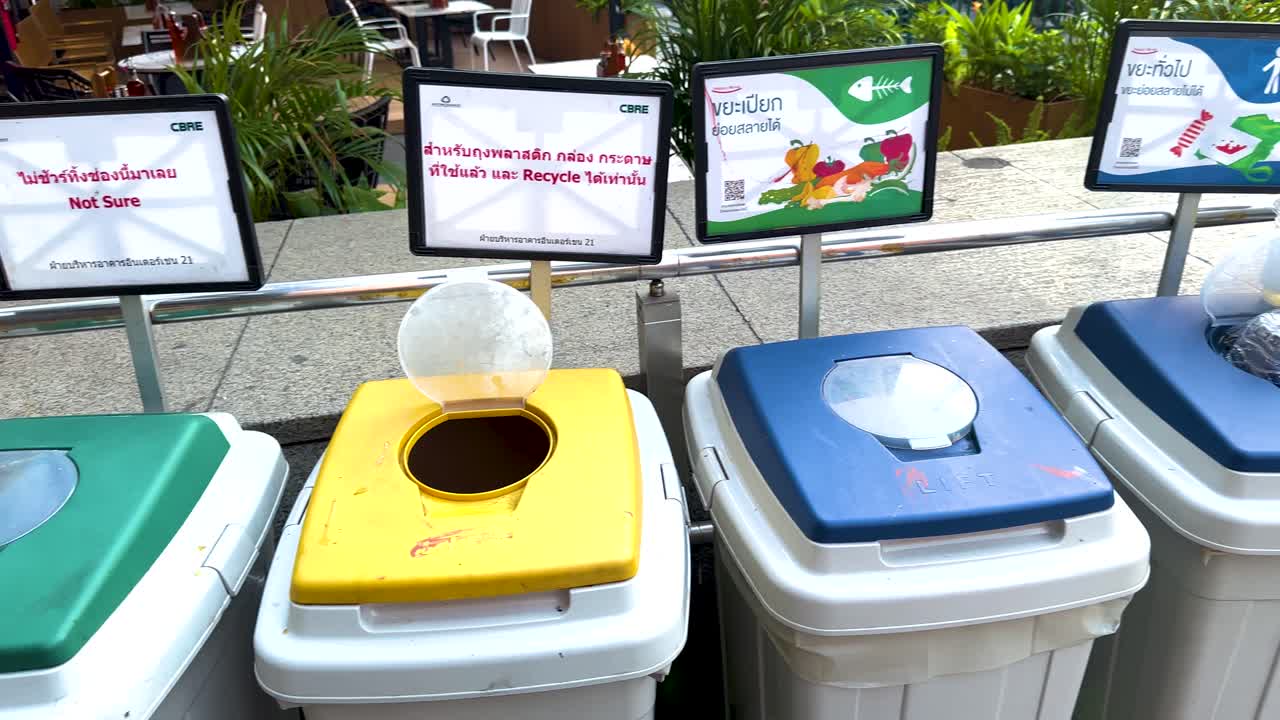 Sequence of recycling bins with distinct colored lids and signage in an outdoor setting, highlighting waste sorting in Bangkok
