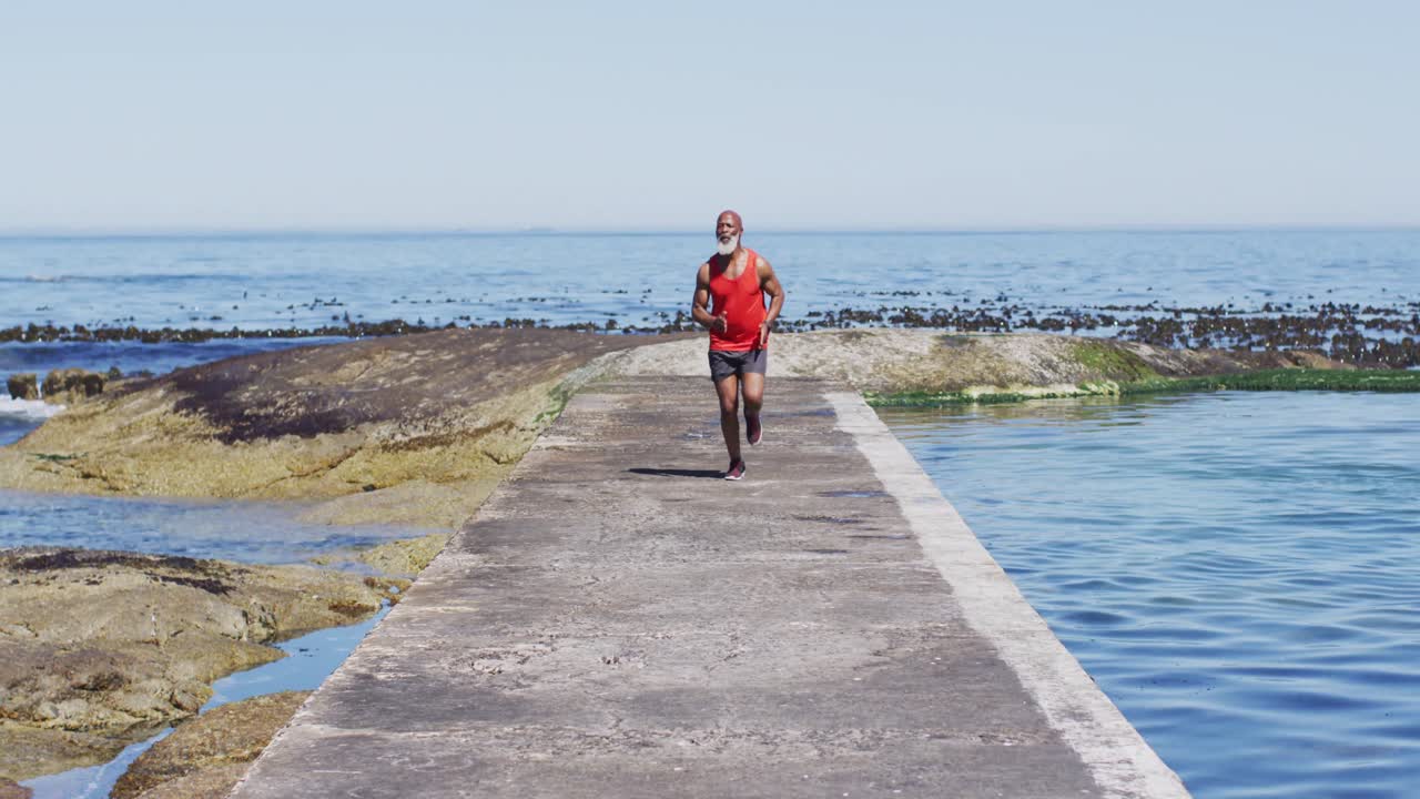 hombre afroamericano senior haciendo ejercicio corriendo en la carretera junto al mar