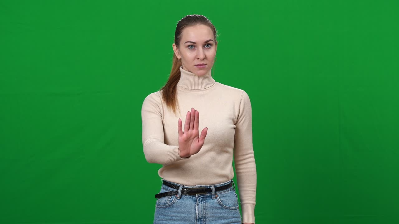 mujer joven estirando la mano a la cámara mostrando gesto de parada y sacudiendo la cabeza no. retrato de hermosa dama caucásica negando en chromakey fondo de pantalla verde