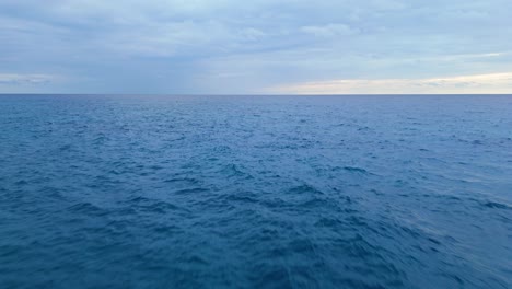 Schnelle-Niedrige-Luftaufnahme-Mit-Dolly-Hinaus-Ins-Tiefblaue-Meerwasser-Mit-Gewitterwolkenregen-Am-Horizont