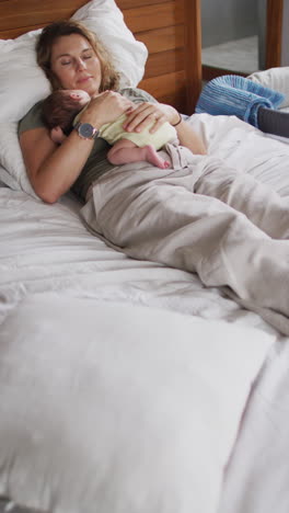 video vertical de una madre caucásica cansada durmiendo con un bebé recién nacido en la cama
