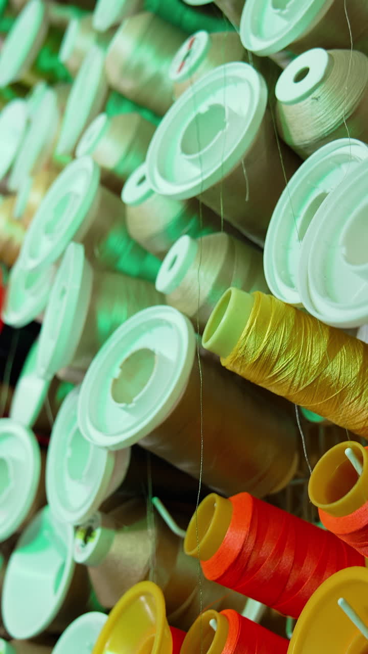 Spools of thread of different colors on the table. Collection of colorful threads for sewing industry. Background of many spools with cotton string. Vertical video