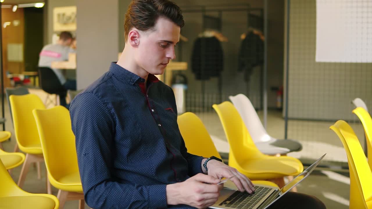 Young attractive guy is using devices. Working on laptop. Co-working space.