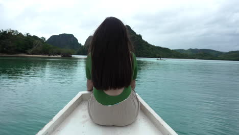 mujer con cabello negro sentada frente a un barco en movimiento en un mar en calma