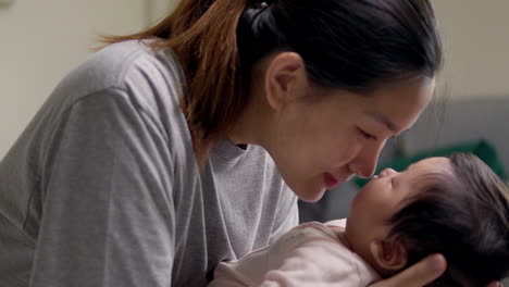mother kissing the forehead of her baby who is sleeping as he cradles her newborn child in her arms.