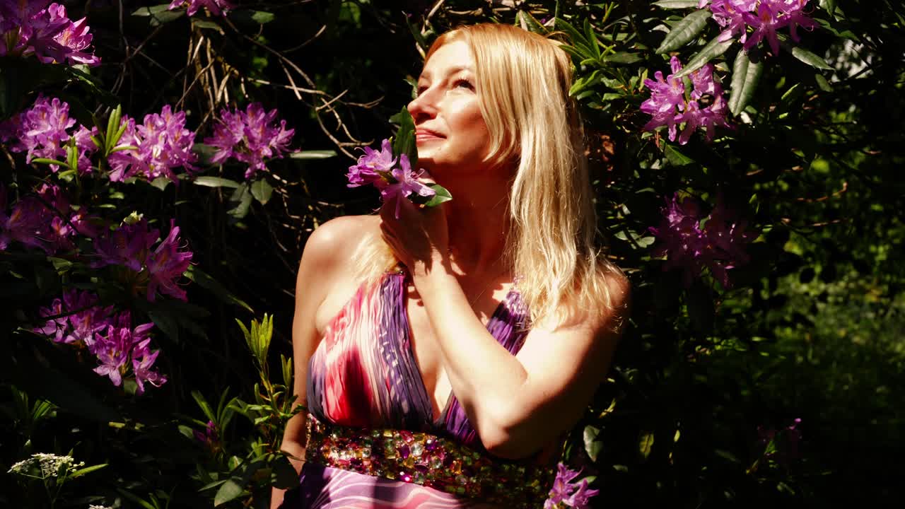 푸른 여름 정원에서 보라색 꽃의 향기를 즐기는 매력적인 여성 중간 초상화 4k 슬로우 모션