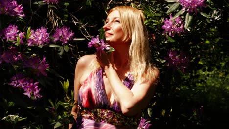 Attractive-woman-enjoying-scent-of-purple-flowers-in-lush-summer-garden-medium-portrait-4k-slow-motion