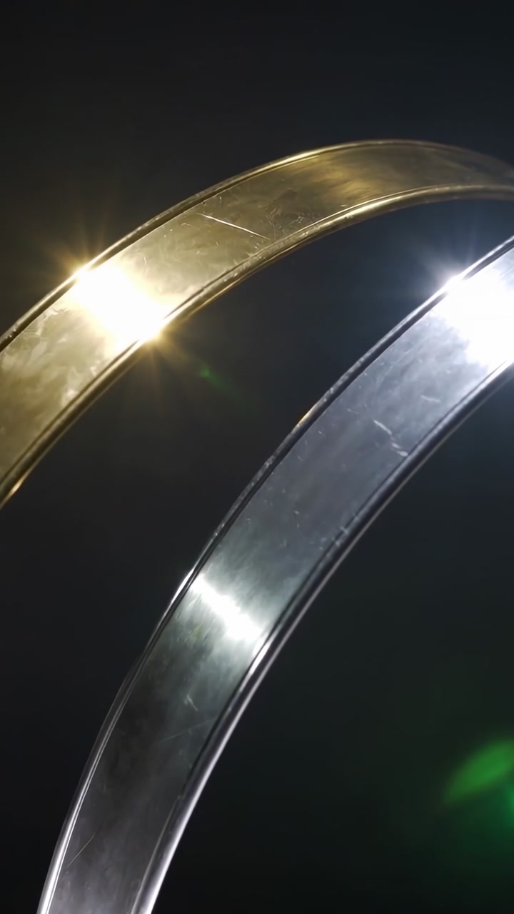 Vertical video: Shifting ray glinting along 2 metal bands in dark room with scratches, green flare