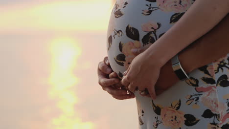 manos masculinas en el estómago de una mujer embarazada solo se ven el estómago y dos pares de manos en