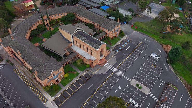 Video ripreso da drone che mostra il tranquillo edificio del Sacro Cuore a Melbourne, con la sua architettura unica, la facciata in mattoni curva e il parcheggio vuoto e simmetrico sotto una luce diurna soffusa