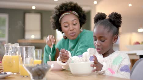 african american mother and daughter eating cereal with milk in kitchen, slow motion