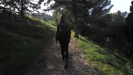 young woman taking a walk on a path among trees, turns back and smiles at camera with the sunlight reflecting, gimbal following