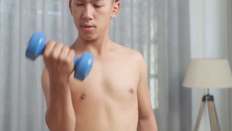 close up of asian teenager boy training with dumbbells while doing shirtless workout at home