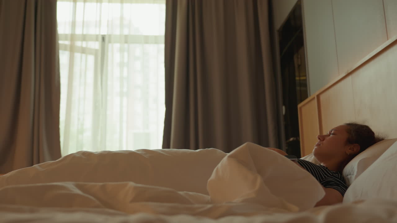 Awal pagi yang cerah. Hotel dengan cahaya matahari menyinari tamu yang sedang tidur. Cahaya matahari terang dari jendela menginspirasi rutinitas bangun yang damai. Tamu yang tidur meregangkan badan ke arah jendela, menampakkan pemandangan kota yang bersinar lembut.