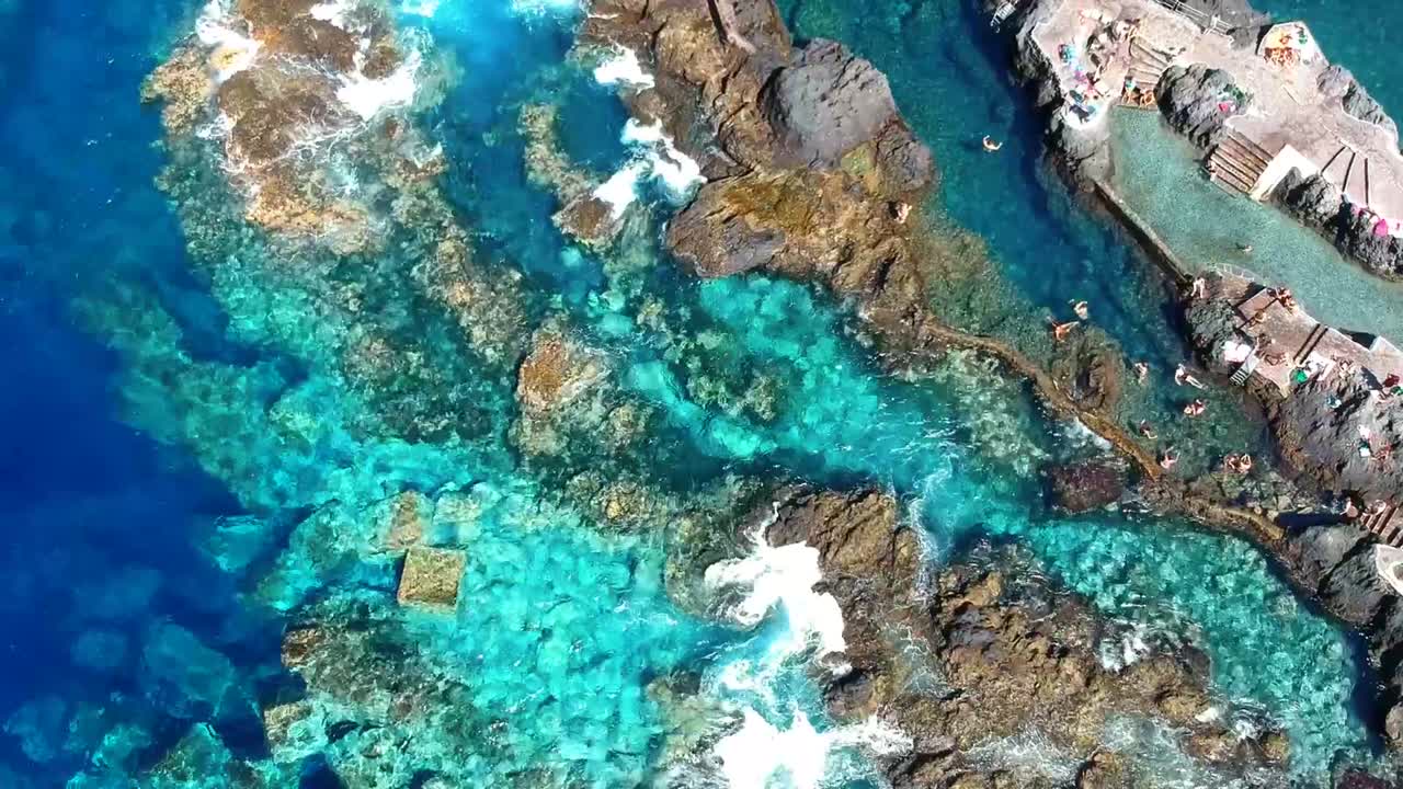 Aerial drone footage of the natural pools of Garachico Caletón. Blue ocean and the natural pools functioning as playas at Tenerife. Nice waves hit the rocks in the water.