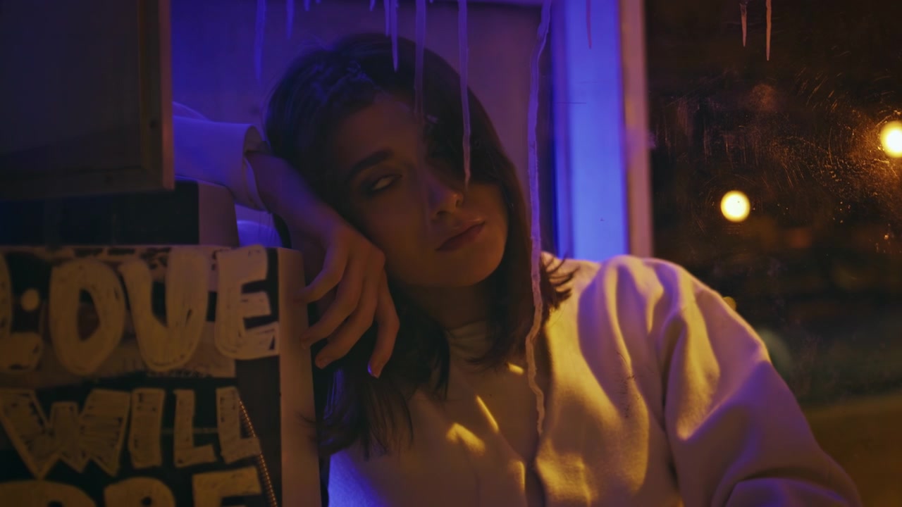 Primo piano di ragazza che appoggia la testa sulla mano, nella notte illuminata da neon viola. Ritratto malinconico alla finestra.