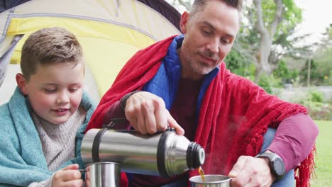 happy caucasian father with son sitting in tent and drinking tea in garden