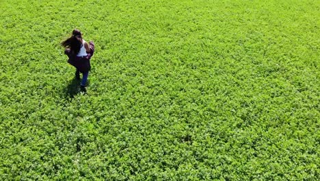 Toma-Aérea-De-Seguimiento-De-Una-Niña-Haciendo-Sus-Propios-Senderos-En-Un-Impresionante-Campo-Verde