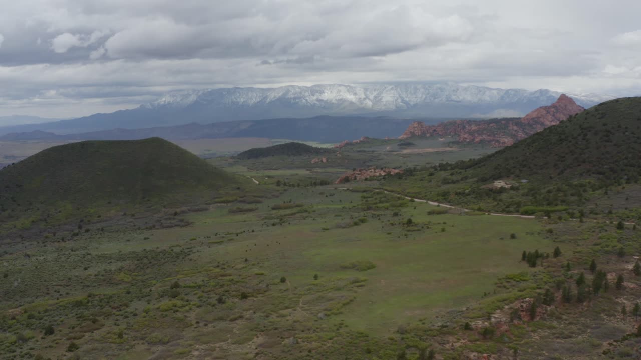 un avión no tripulado volando lentamente sobre campos de hierba, acercándose lejos a las montañas nevadas en el parque nacional de zion