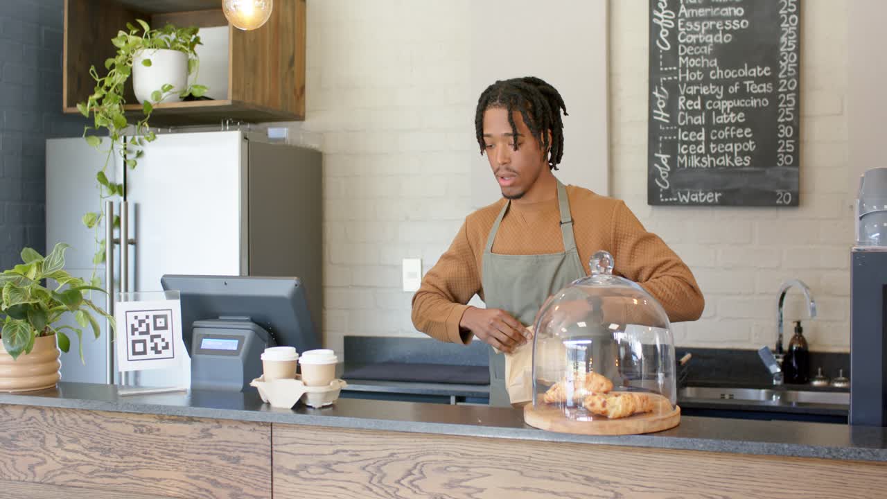 African American male barista reaching for brown bag and packaging at POS counter for pickup