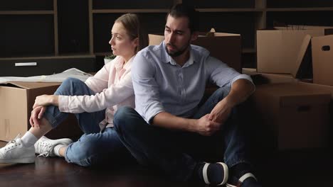 tired unhappy married couple sit on floor with cardboard boxes