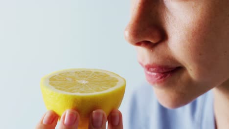 Video-close-up-detail-of-caucasian-woman-smelling-half-cut-lemon,-with-blue-copy-space