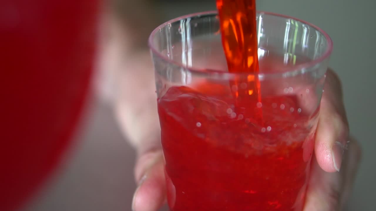 Pouring red drink into clear plastic cup.
