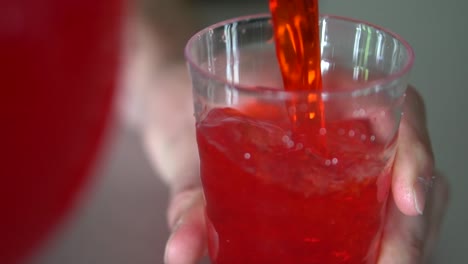 pouring red drink into clear plastic cup.