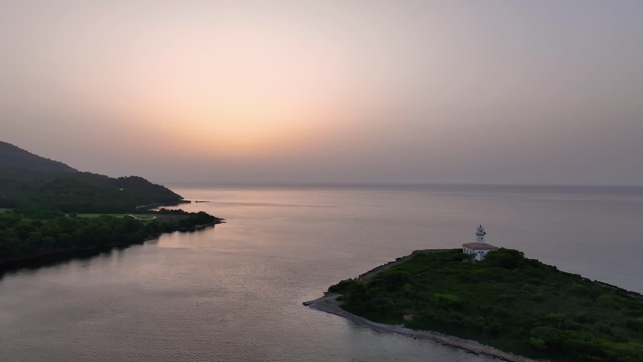 작은 섬의 등대와 함께 해상에서 해가 뜨는 쪽으로 날아가는 드론