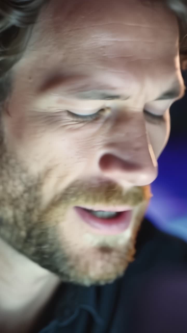 Primi Piani di un Uomo Pensieroso con Occhi Blu Intensi e una Barba Elegante in un Ambiente Illuminato Delicatamente, Catturando Momenti di Contemplazione e Concentrazione