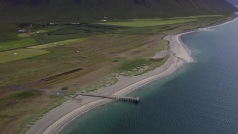 Luftüberflug-über-Weißen-Sandstrand-Mit-Steg-Und-Meerwasser-Neben-Grüner-Landschaft-Auf-Island-–-Weitwinkelaufnahme