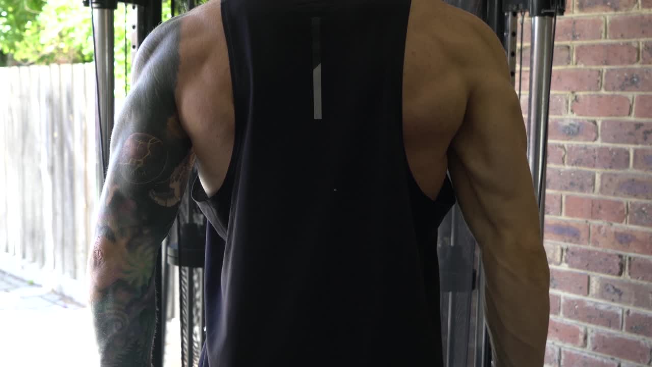 hombre musculoso en el gimnasio en casa haciendo ejercicio con un solo cable de brazo tirando hacia abajo