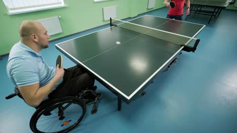 a man in a wheelchair plays ping pong. people with disabilities play table tennis. rehabilitation of the disabled. paralympic sport.