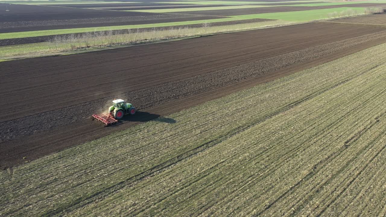 vista lateral aérea de un tractor que arrastra un cultivador de semilleros por un campo agrícola, tierras de cultivo