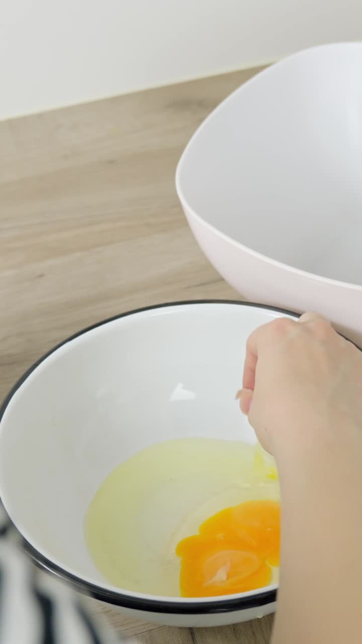 Close-up vertical shot of an egg cracked into a mug, eggshell dropping, for tiramisu preparation.