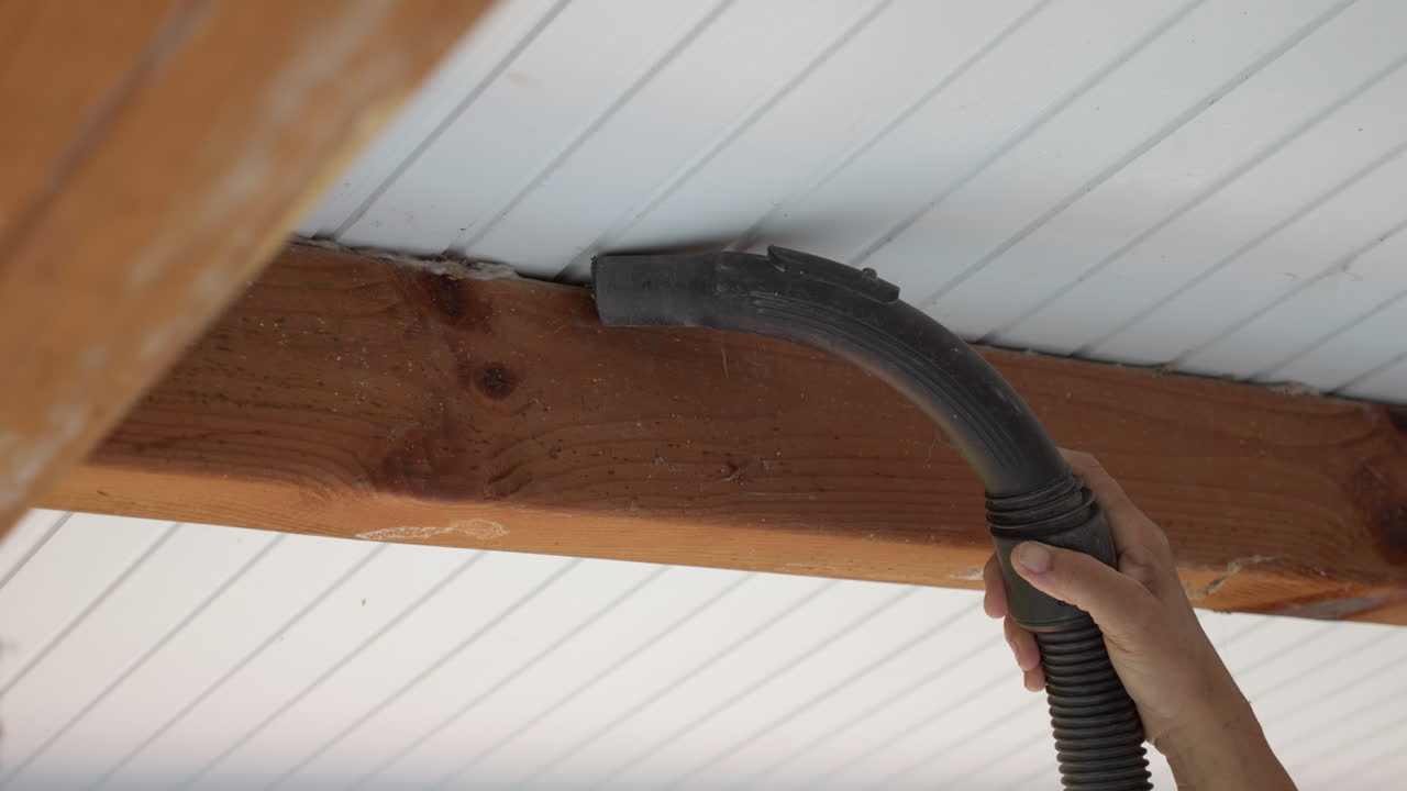 Person vacuuming cobwebs from the ceiling beams of a house. Close up