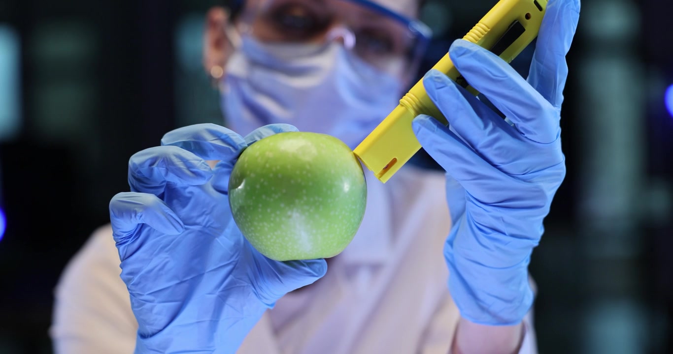 Scienziata controlla una mela verde con un tester giallo in laboratorio.