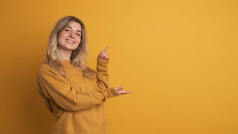cheerful young woman showing side space with fingers on yellow background