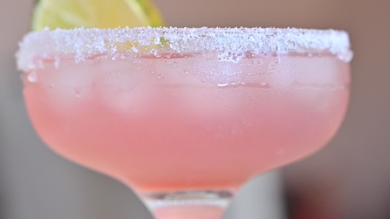 Primer plano de un cóctel rosa claro con hielo y rodajas de lima