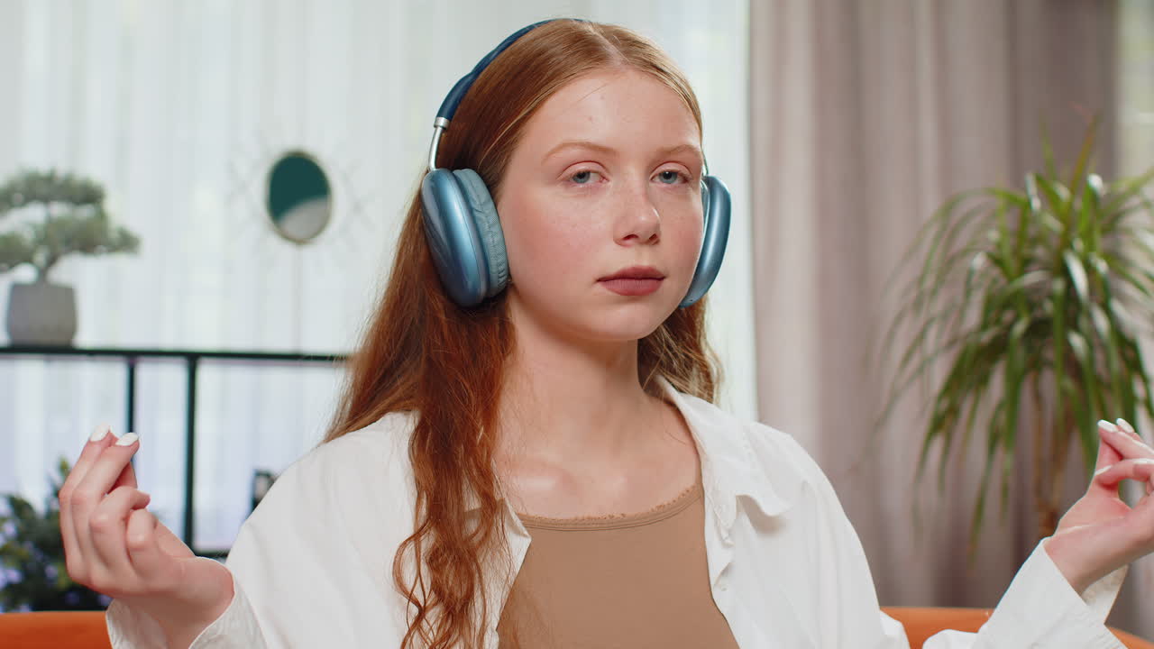 Teenager red hair girl breathes deeply with mudra gesture eyes closed meditating listening music